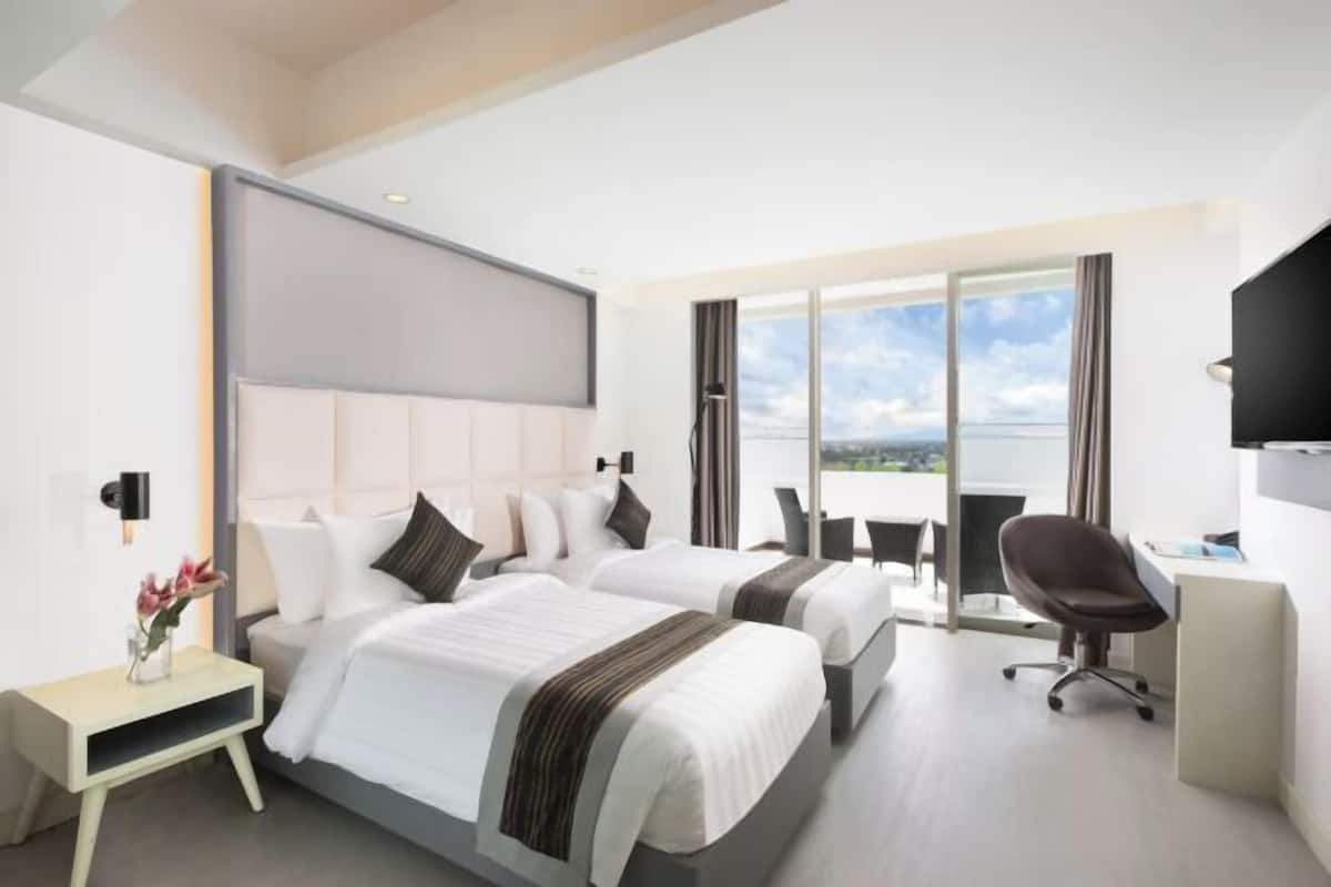 Une chambre d’hôtel avec deux lits, un bureau, une chaise et une grande fenêtre donnant sur un beau paysage.