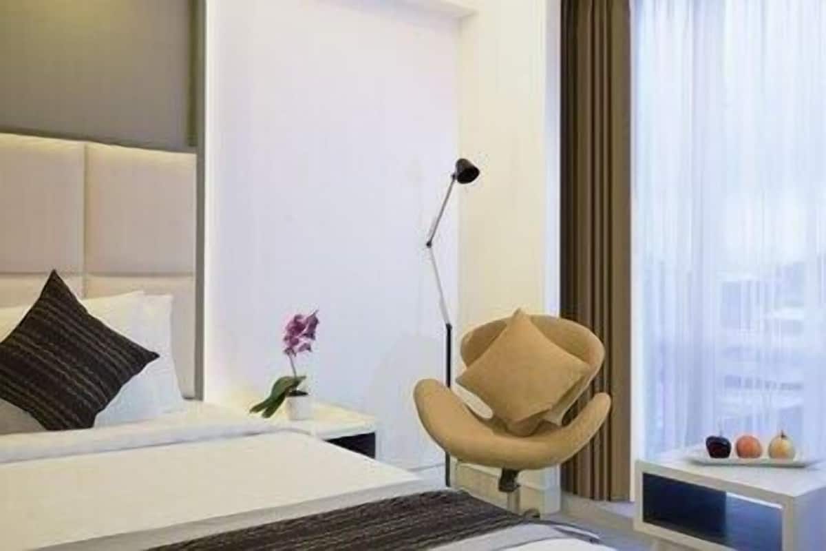 Une chambre d’hôtel moderne, équipée d’un lit, d’une chaise, d’une table de chevet, d’une lampe et d’une fenêtre avec des rideaux.