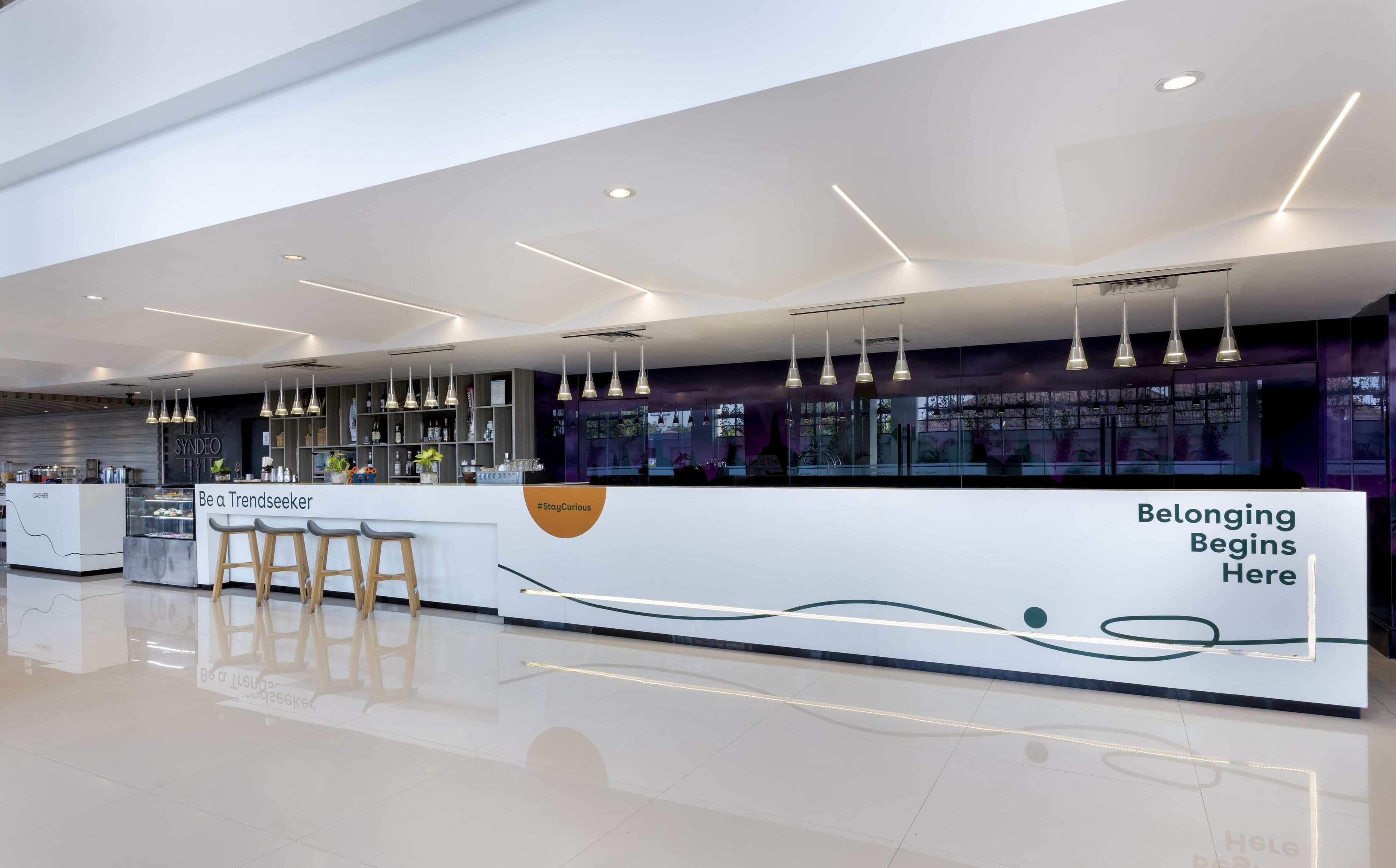 Un área de recepción moderna y bien iluminada, con mostrador, taburetes tipo bar y una vitrina de vidrio.