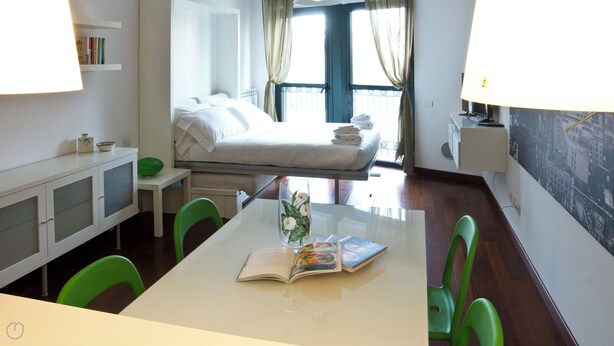 Ein Hotelzimmer mit einem Bett, einem Schreibtisch mit Stühlen, einem Bücherregal und einem Fenster mit Vorhängen.