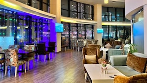 A modern hotel lobby with a bar area, seating arrangements, and large windows offering city views. - Sky Tower Hotel (Batumi)