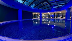 An indoor swimming pool with a glass ceiling, lounge chairs, and a tiled floor. - Sky Tower Hotel (Batumi)