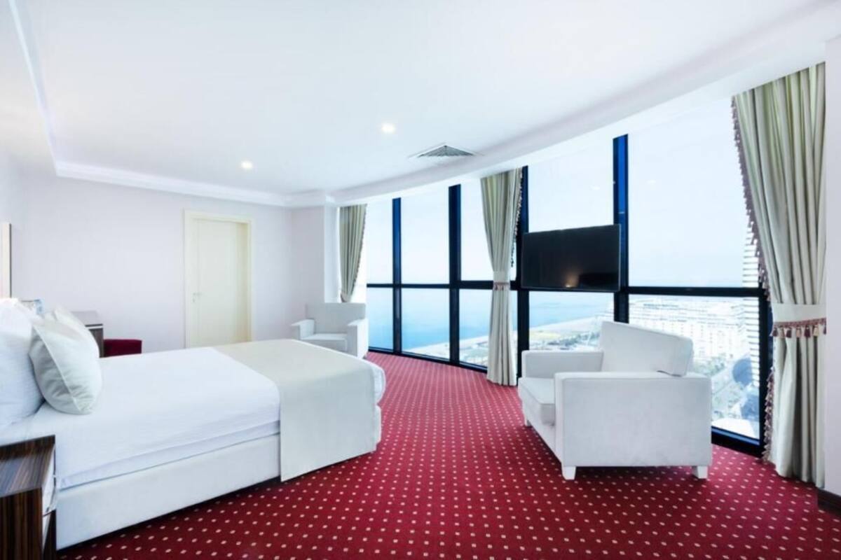 A hotel room with a bed, a sofa, and a large window offering a city view.