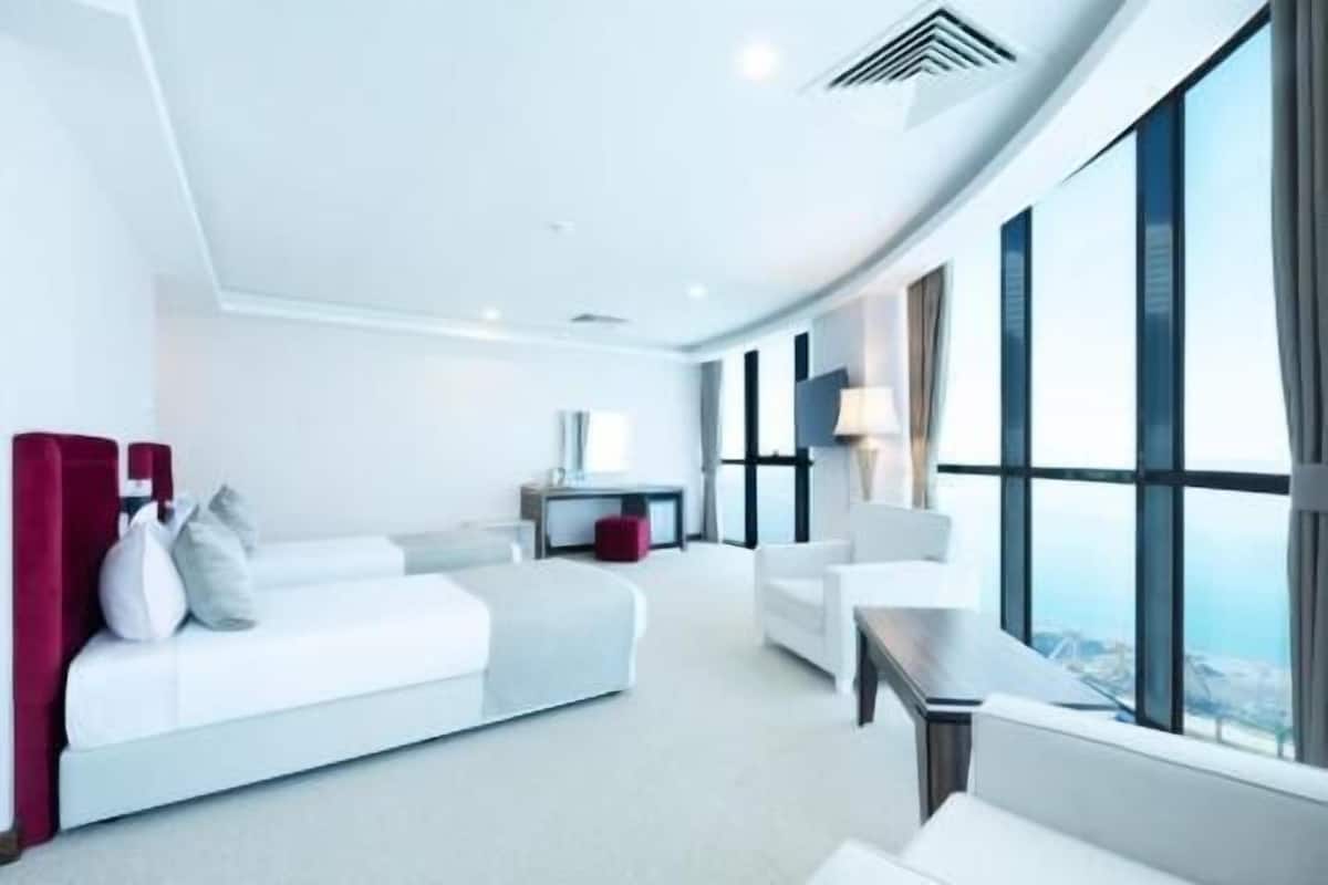 A modern hotel room with a curved ceiling, a large window, a white sofa, a small table, and a desk.