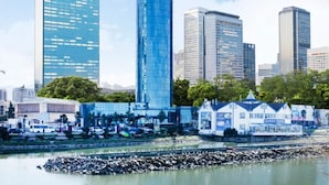 A cityscape with modern high-rise buildings, a waterfront area, and a small house-like structure with a sign. - Sky Tower Hotel (Batumi)
