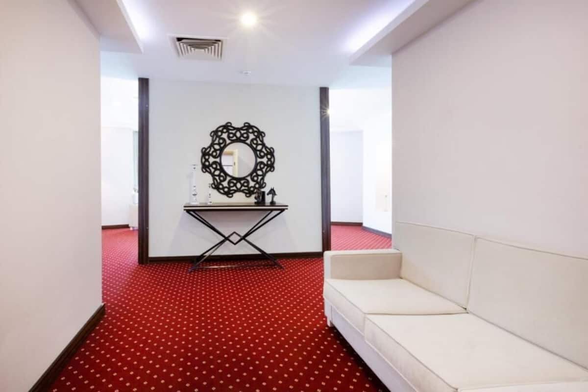 A room with a red carpet, a white sofa, a table with a mirror, and a wall-mounted decorative piece.