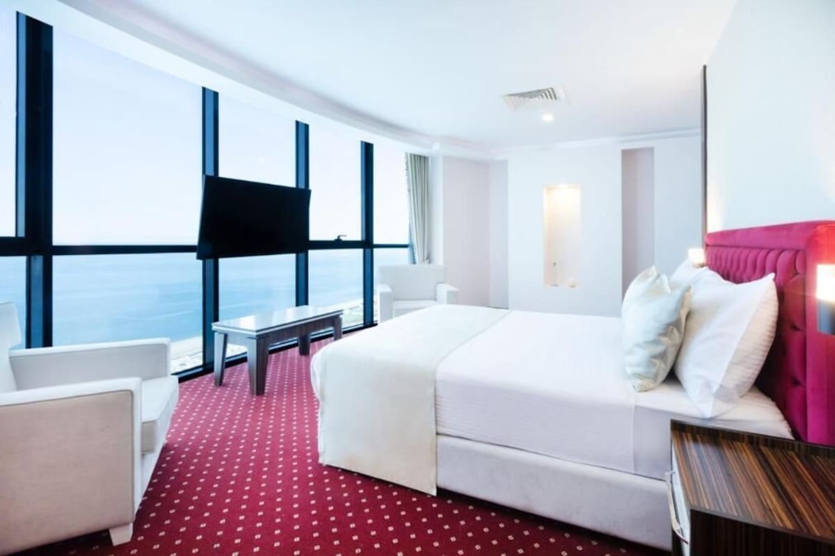 A hotel room with a large bed, a desk, a chair, a TV, and a window with a view.