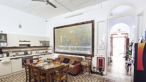 A kitchen with a dining table, chairs, a sofa, and a large painting on the wall. - Granny's Inn - Hostel (Sliema)