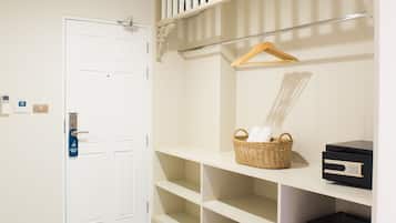 Habitación de hotel con puerta blanca, tocador blanco con estantes, cesta con toallas y electrodoméstico negro.