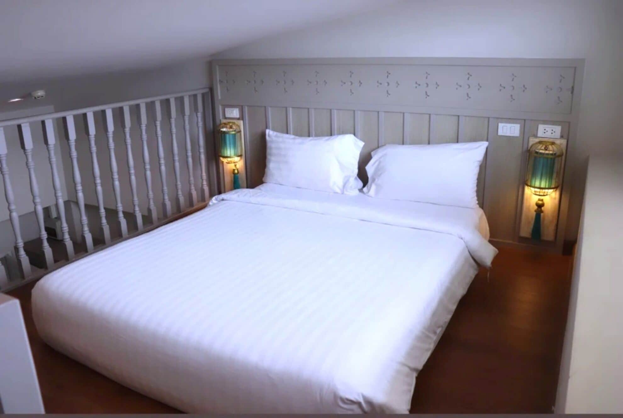 Ein ordentlich bezogenes Bett mit weißen Laken in einem Zimmer, das ein hölzernes Kopfende und zwei Wandleuchten hat.