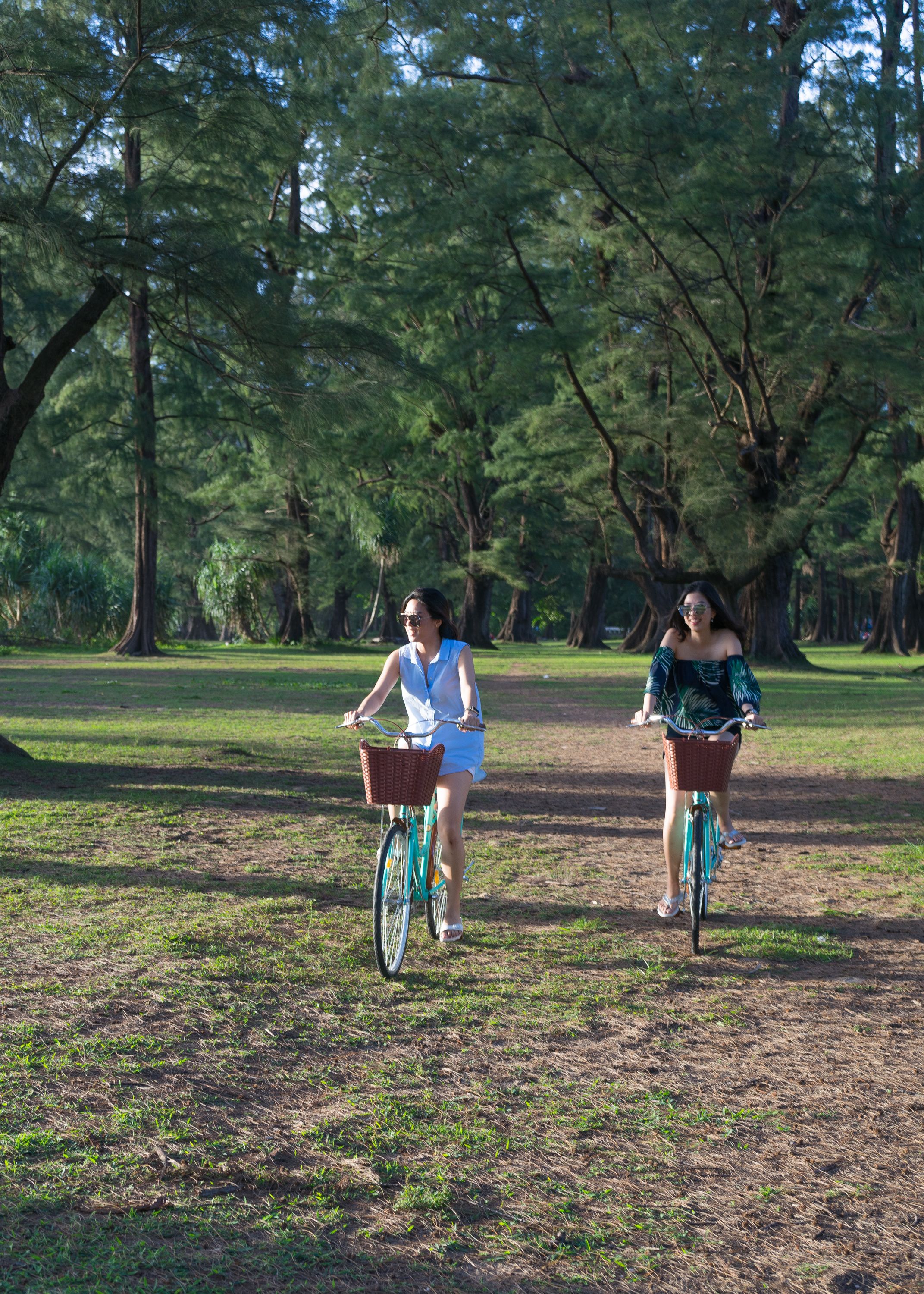 Dos personas montando en bicicleta en un parque con árboles y césped.