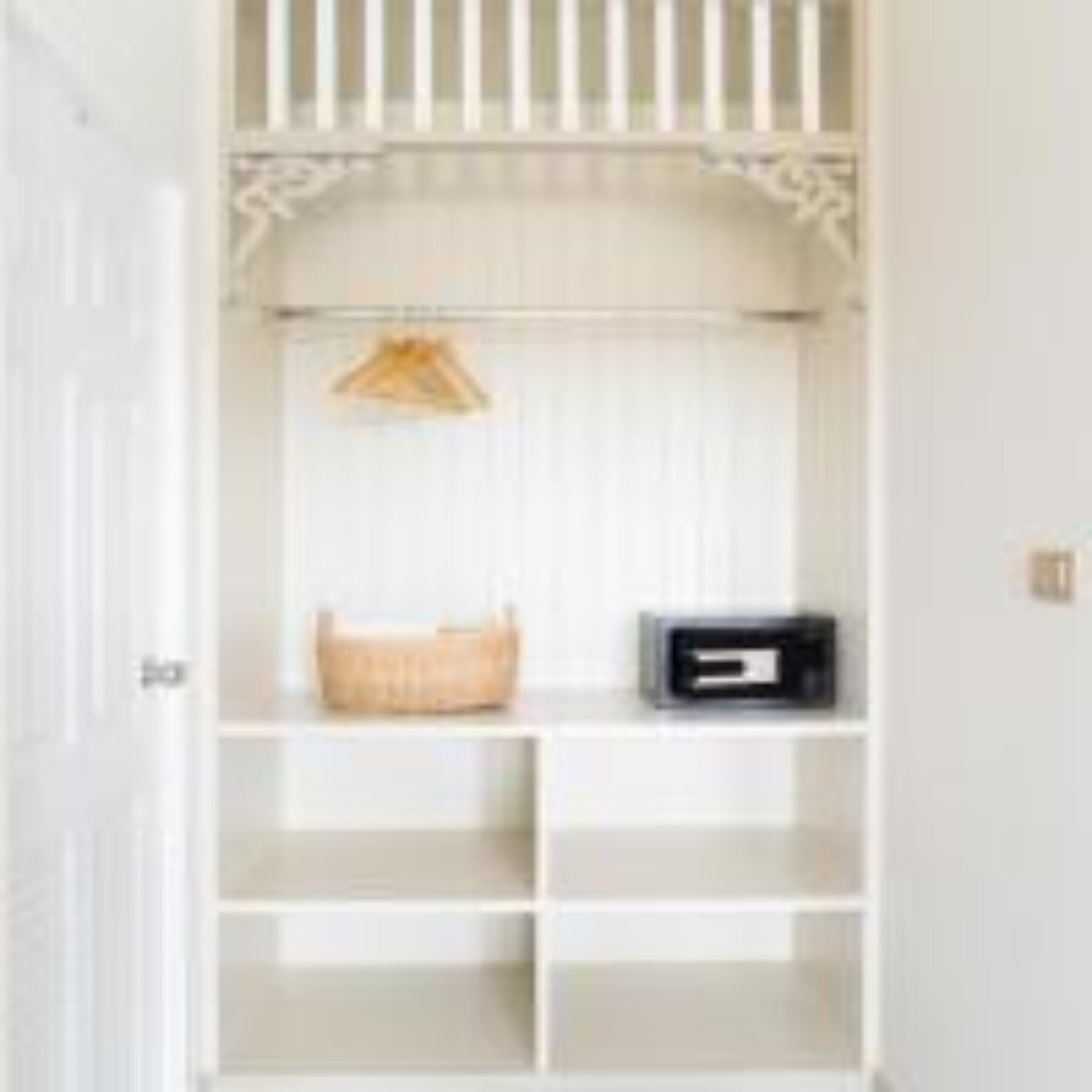 A white closet with open shelves, a hanging basket, and a black storage box.