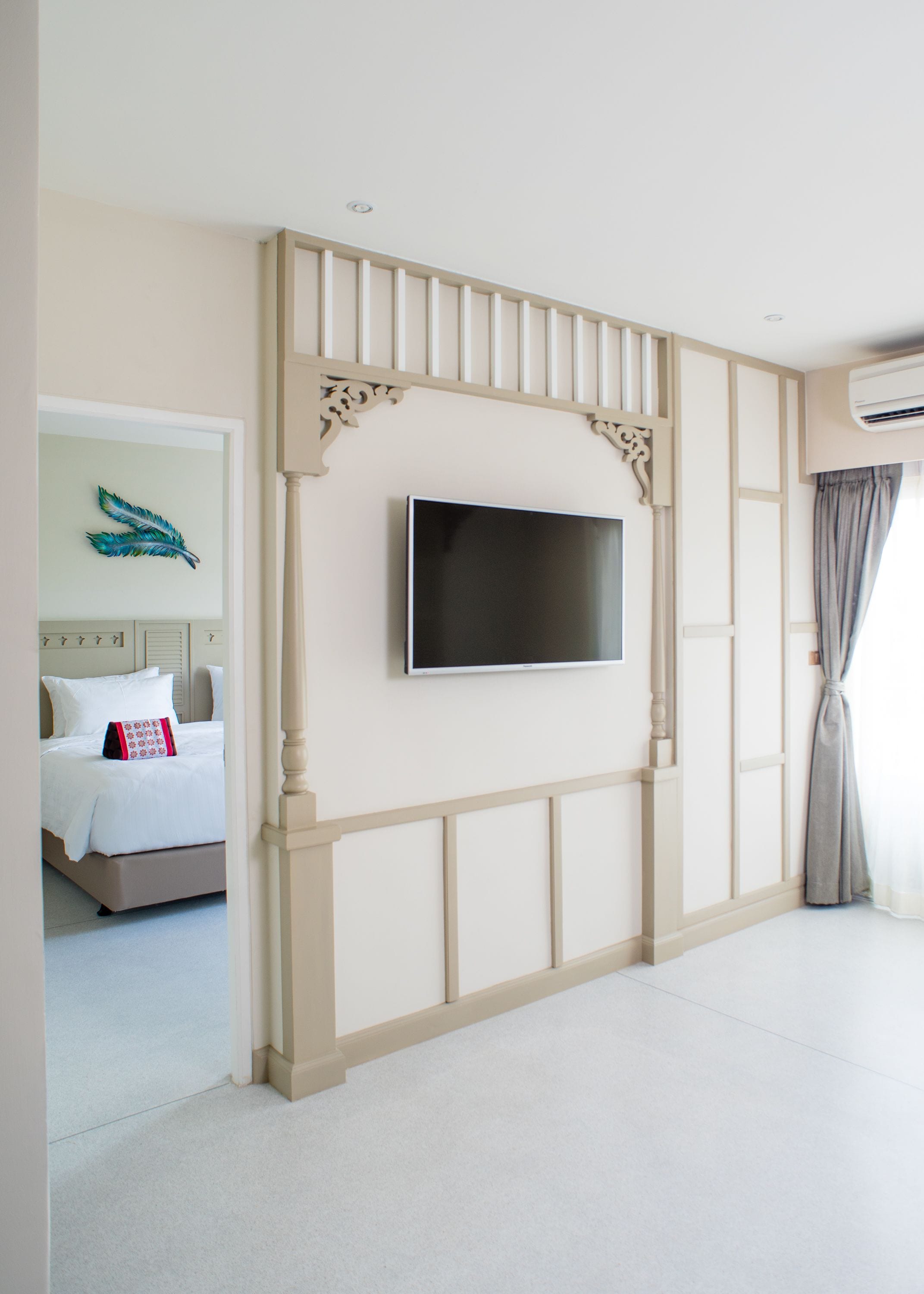 A hotel room with a bed, a flat-screen TV mounted on a decorative wall, and a window with curtains.