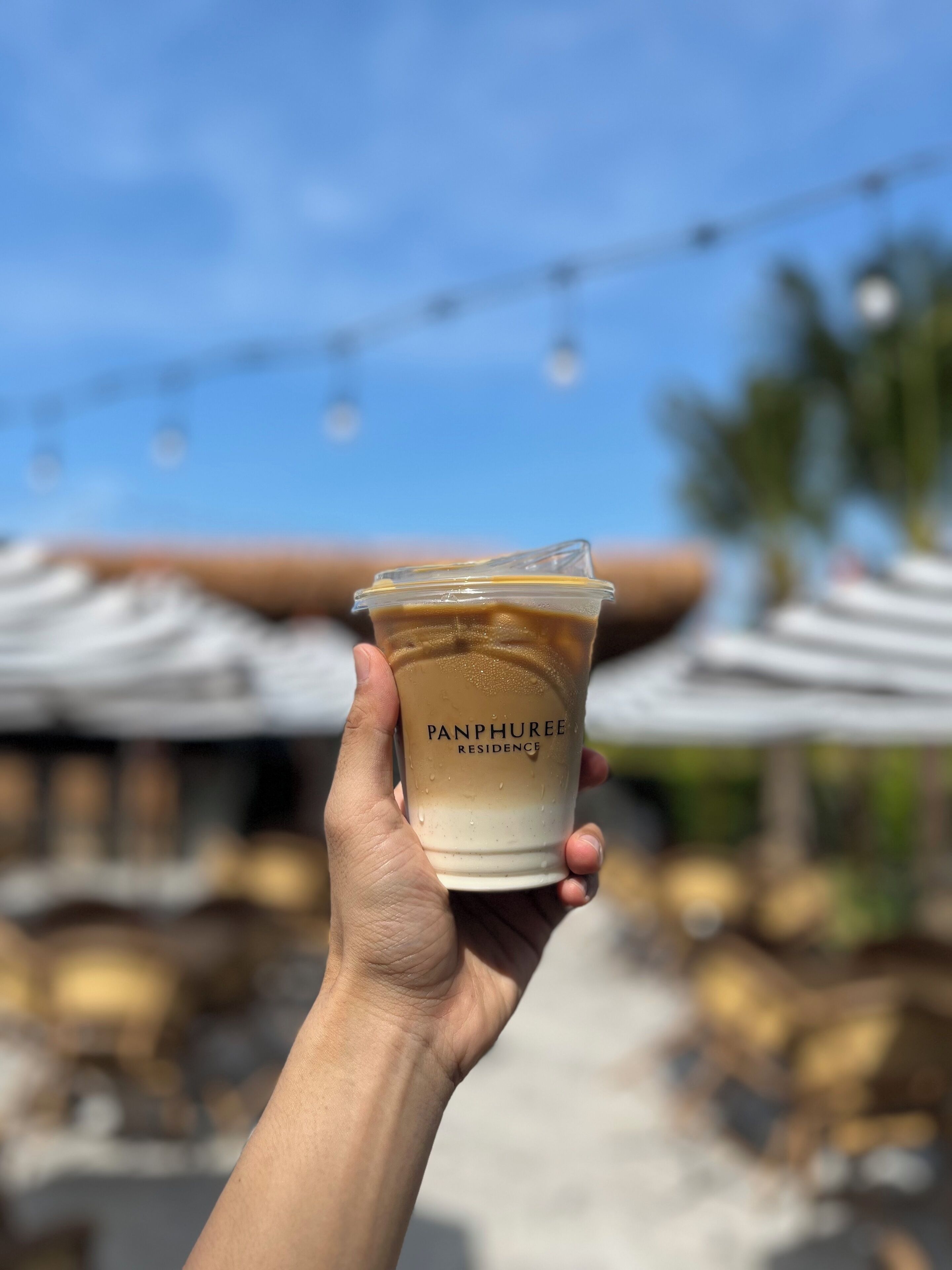 A hand holding a Panphuree Residence branded drink cup.