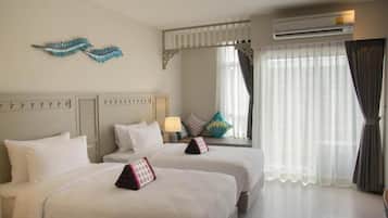 A hotel room with two beds, a window with sheer curtains, an air conditioning unit, and decorative wall art.