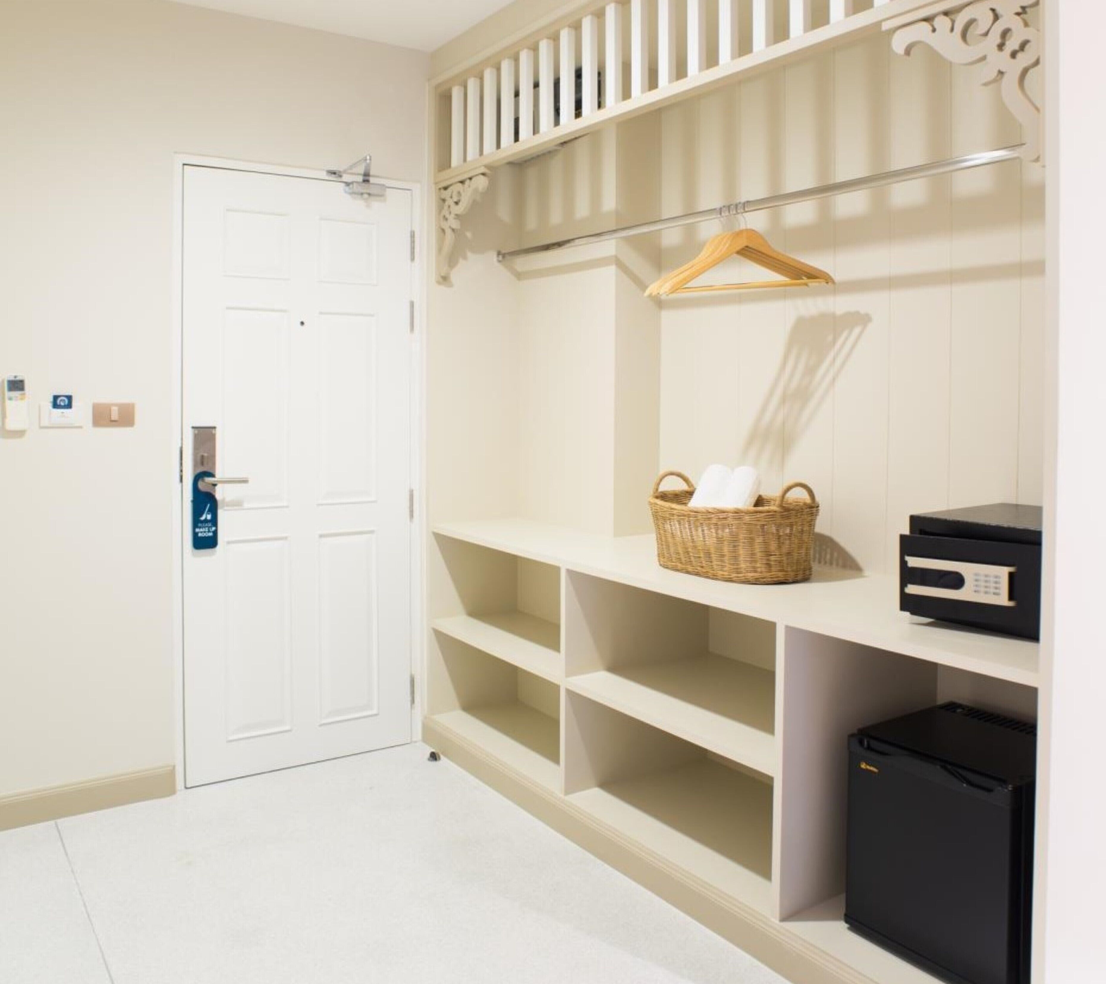A clean, white hallway with a door, a white shelving unit with a basket and a black device, and a small black trash bin.