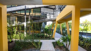 Un espace extérieur doté d’un chemin en béton, de piliers de soutien jaunes et de plantes vertes.