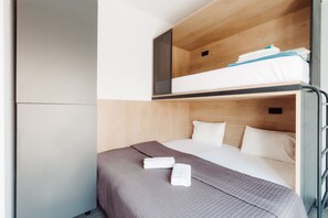 A bunk bed room with a grey quilted bedspread, white pillows, and neatly folded towels.