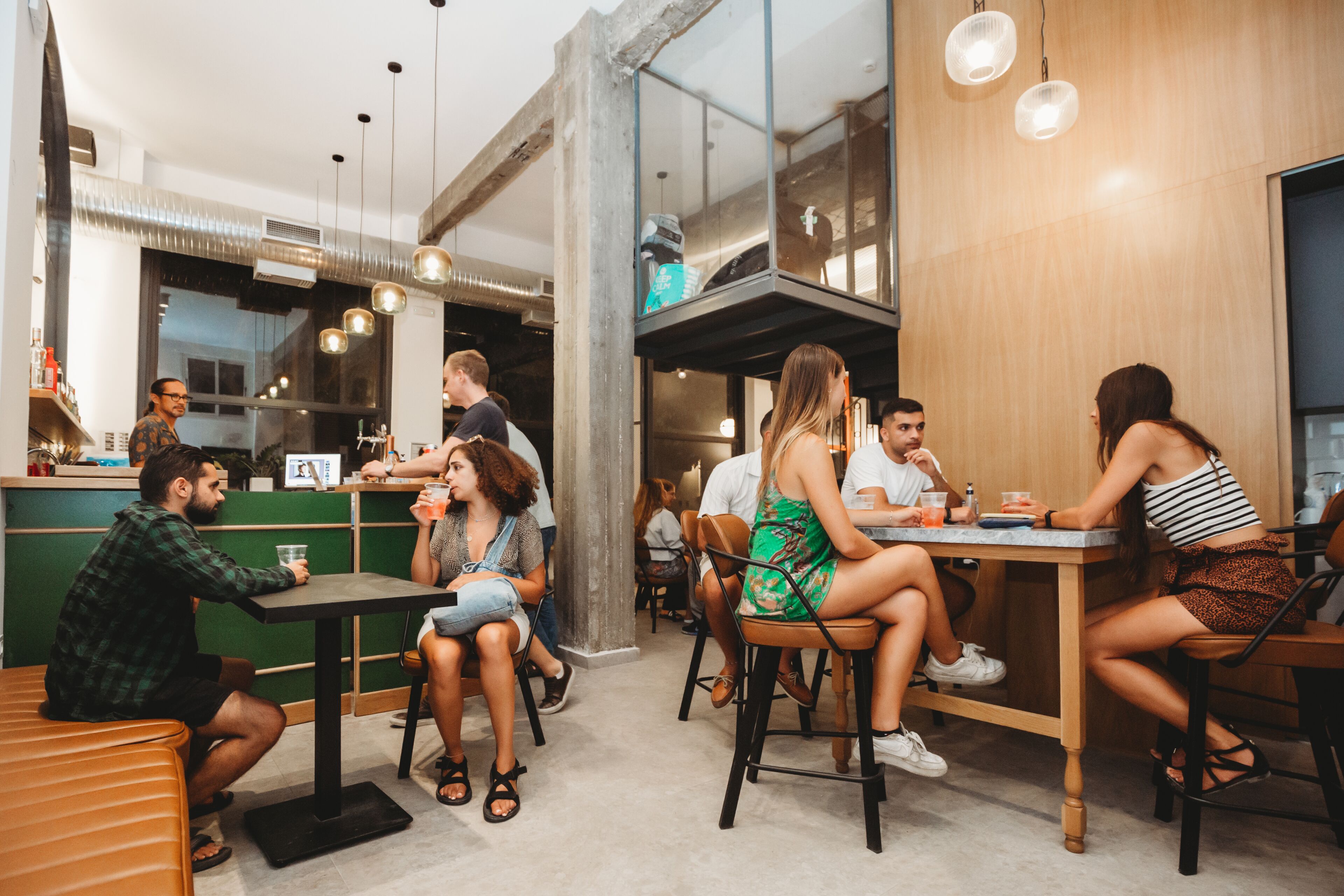 A modern cafe with multiple tables and chairs, a counter with a menu, and a visible kitchen area.