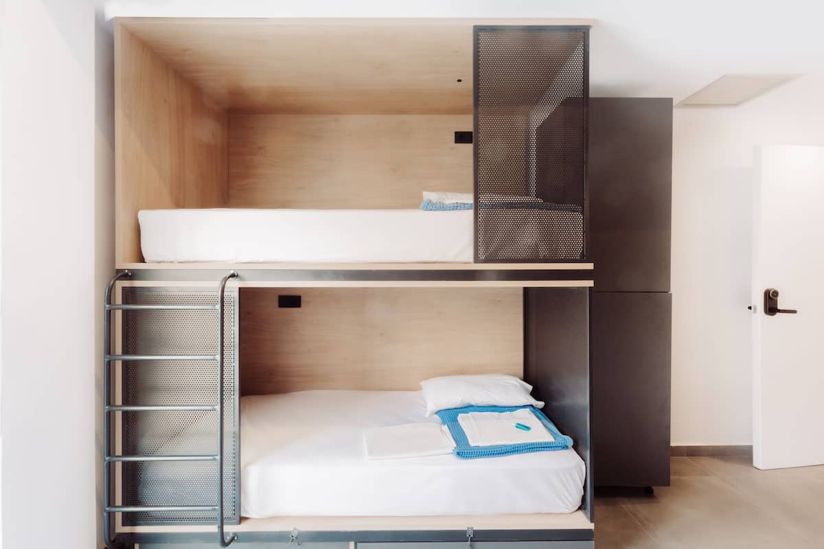 A bunk bed with a metal ladder, a white mattress, and a blue blanket.