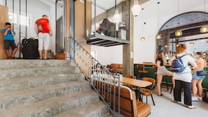 A staircase leading to a seating area with tables and chairs, a bar area with stools, and a mezzanine level with hanging lights.