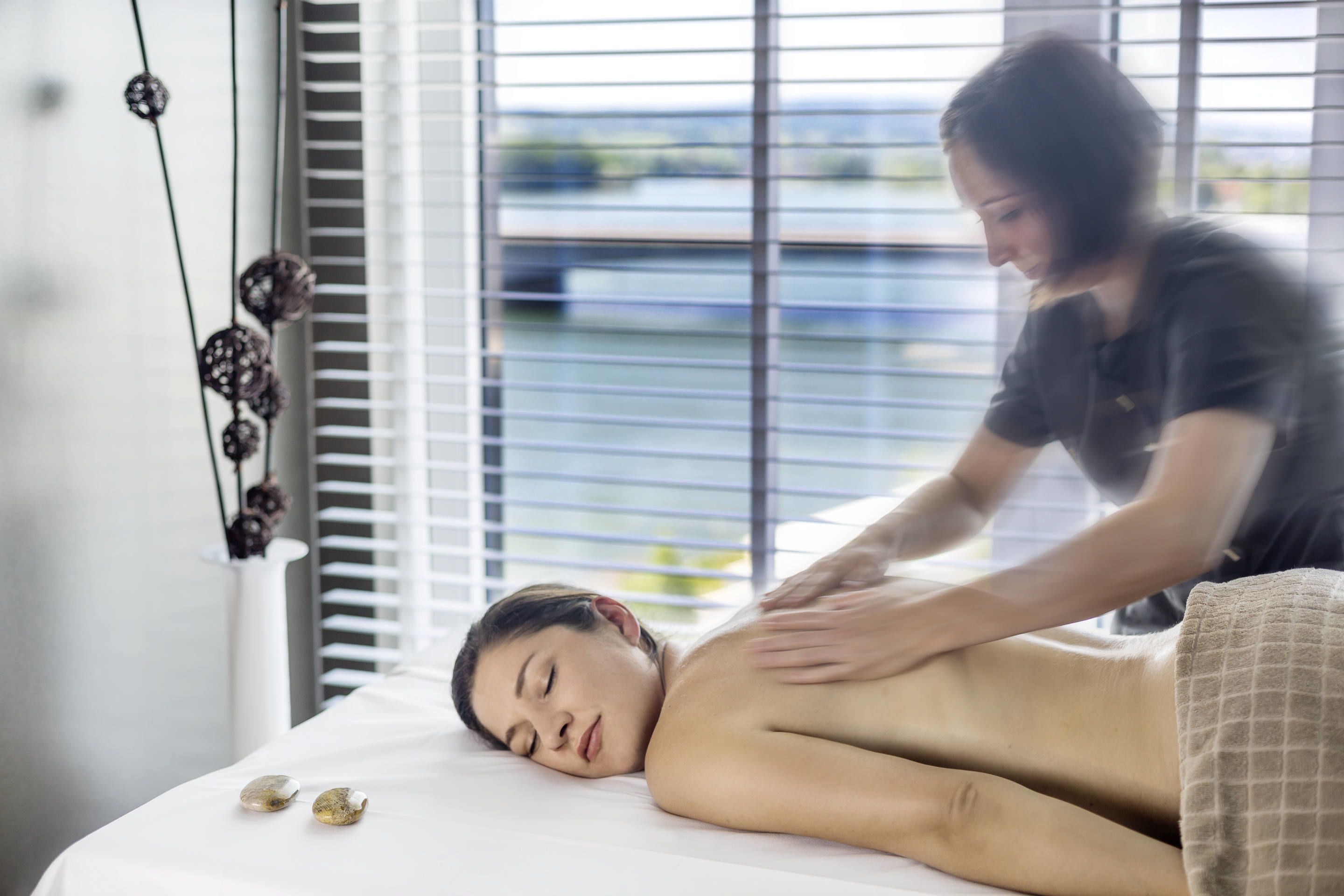 A massage therapy session in a room with a bed, a window with blinds, and a decorative string of beads.
