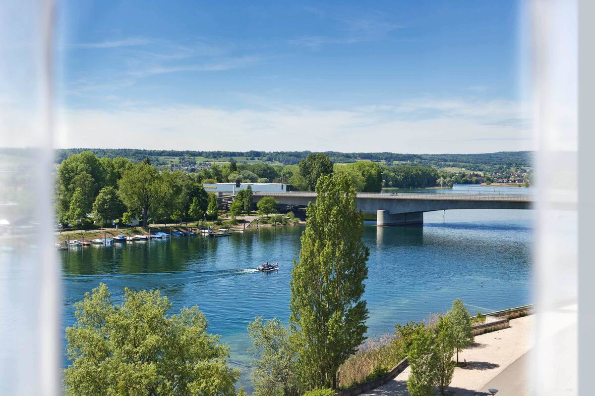 Un río con un puente, barcos y árboles.