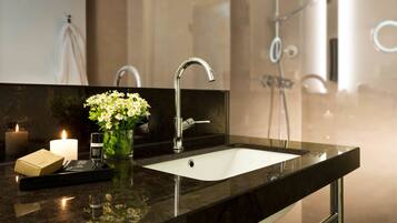 A modern bathroom with a black marble sink, a glass vase with flowers, a lit candle, and a small box.