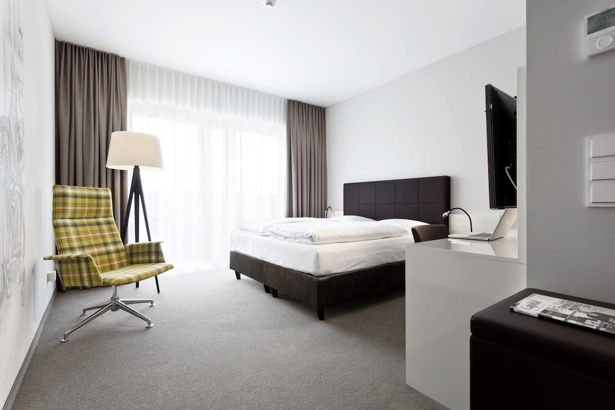 Una habitación de hotel con una cama, un escritorio con una computadora portátil, una silla, una lámpara y un televisor.