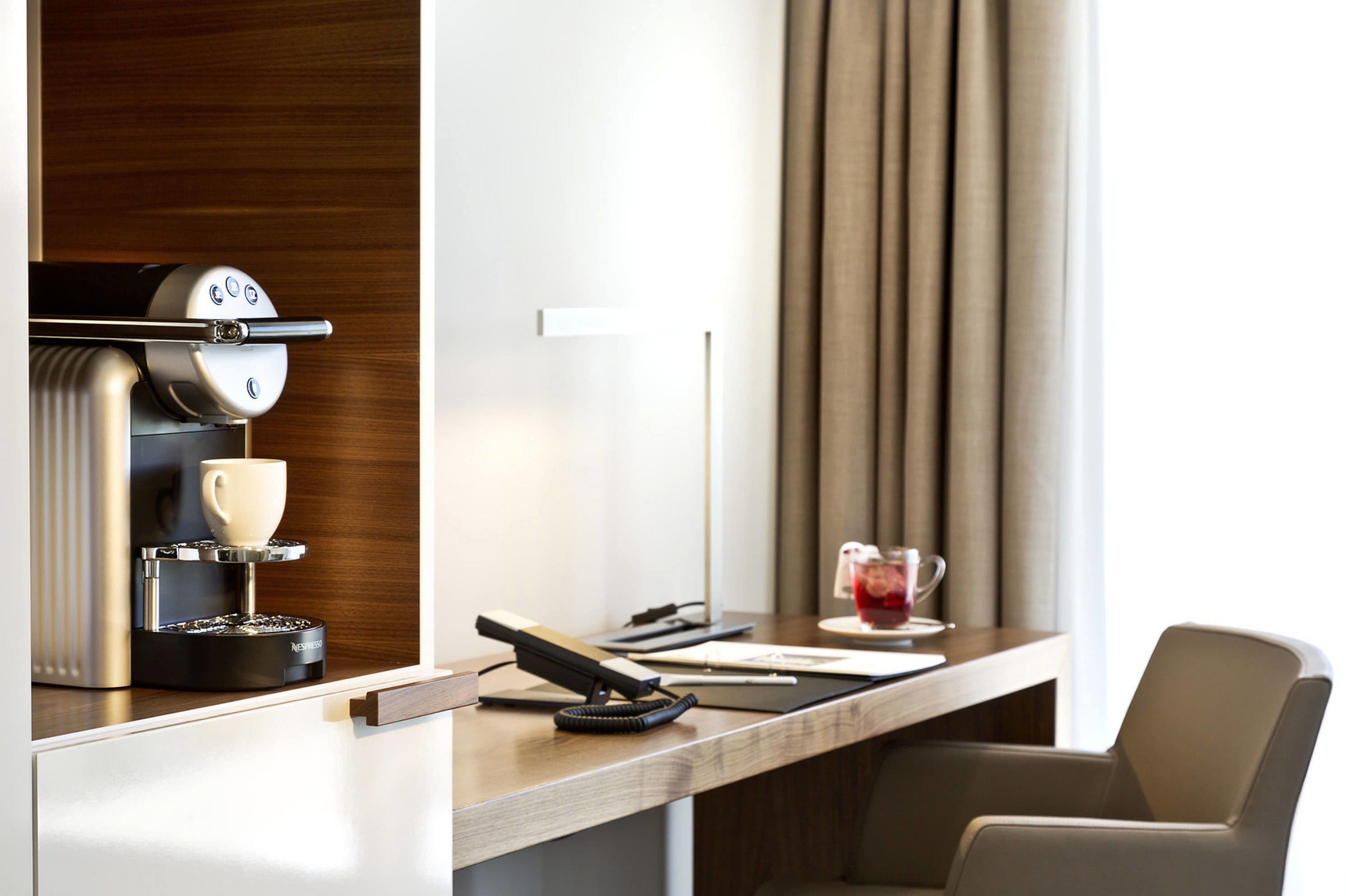 A modern hotel room with a built-in espresso machine, a desk with a telephone, and a chair.