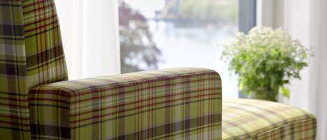 Un sillón estampado con diseño escocés junto a una ventana con vistas a un río y edificios.