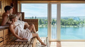 Een houten sauna met grote ramen met uitzicht op een rivier en stadsbeeld.