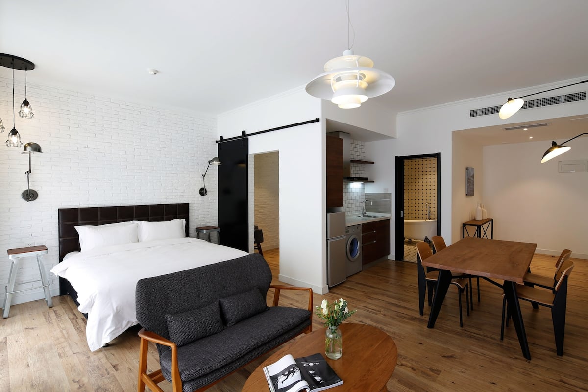 Un dormitorio moderno con una cama grande, un sofá, una mesa de comedor con sillas, una lavadora y una zona de cocina.