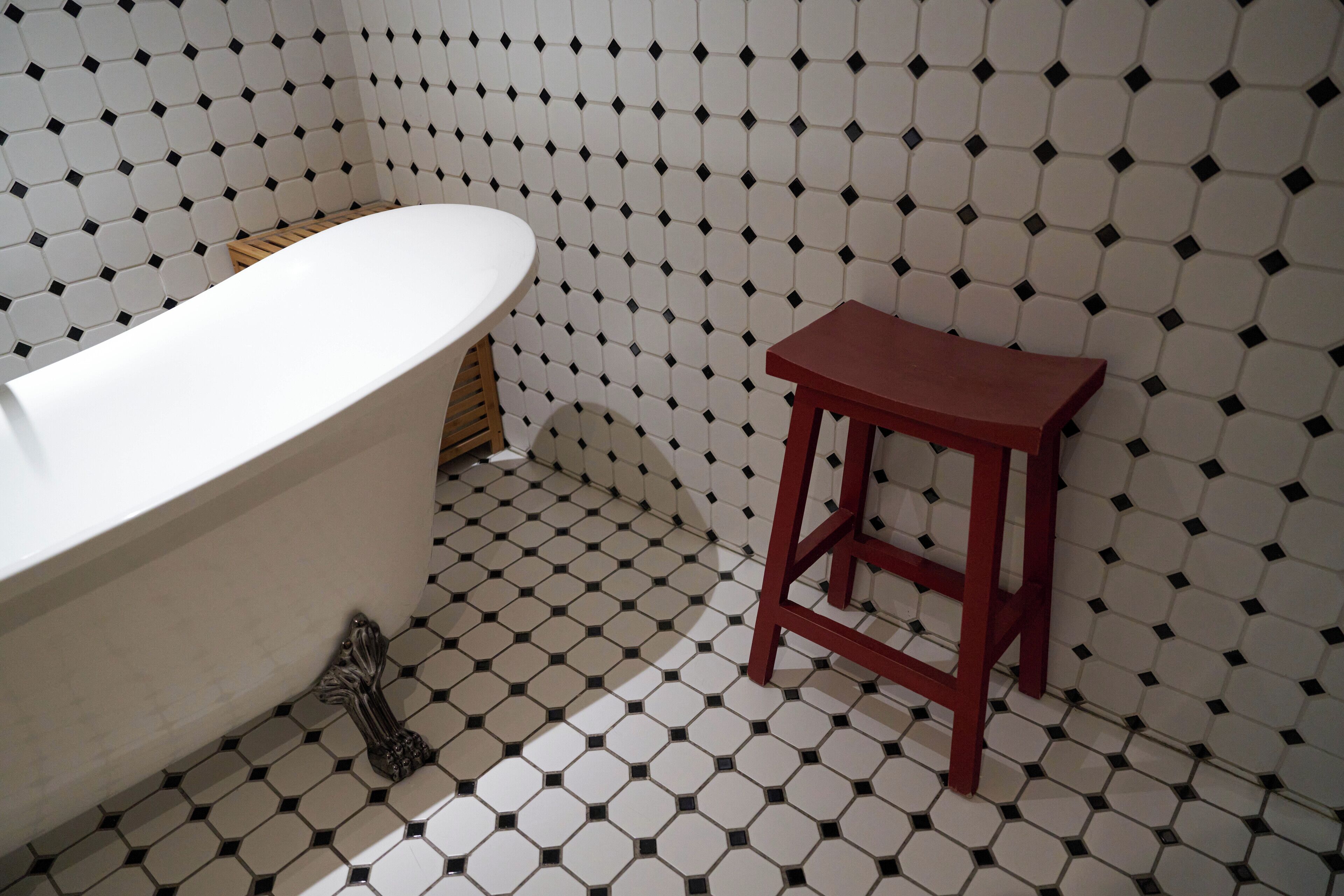 Une salle de bain avec une baignoire blanche, un tabouret en bois et un sol carrelé orné d’un motif géométrique.
