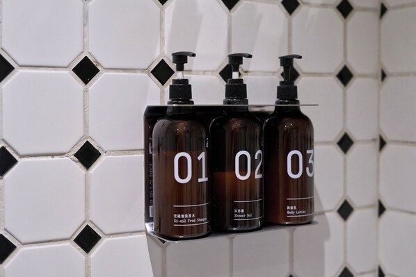 Three bottles of body lotion on a shelf against a tiled wall.