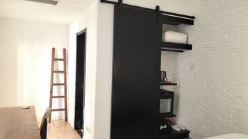 Un dormitorio con cama, armario de puertas correderas, escalera de madera, escritorio y pared de ladrillo blanco.