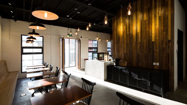 Uma sala de jantar moderna com mesas e cadeiras de madeira, iluminação pendente e bancada de cozinha.