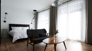 Quarto moderno com cama, sofá escuro, mesa de madeira redonda e parede de tijolos brancos.