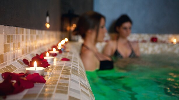 A row of candles and rose petals on a tiled ledge beside a pool area. - Hotel Palisad (Zlatibor)