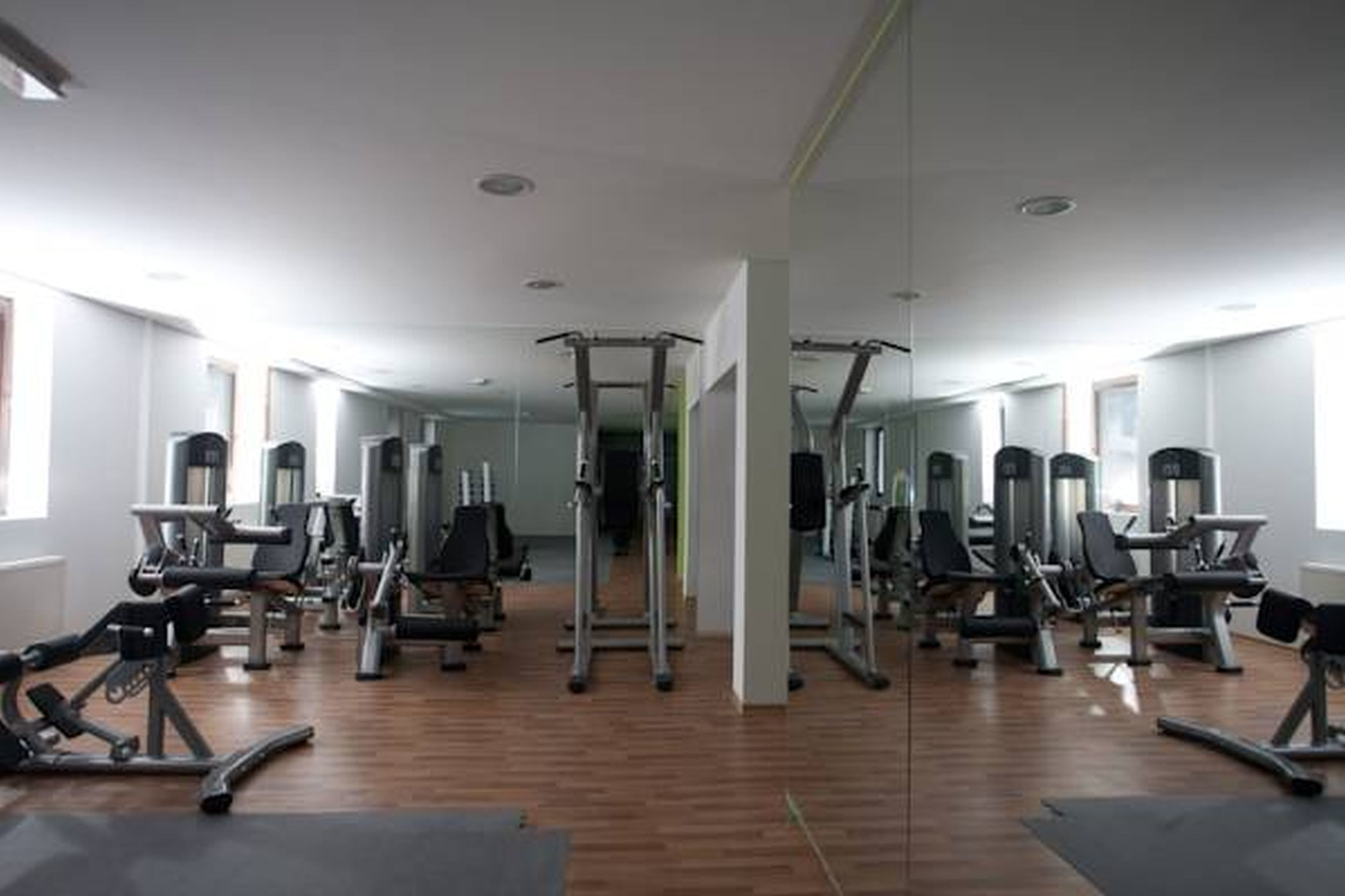 A gym with various exercise machines, wooden flooring, and large windows.