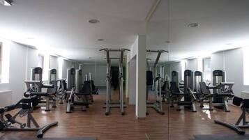 A gym with various exercise machines, wooden flooring, and large windows.