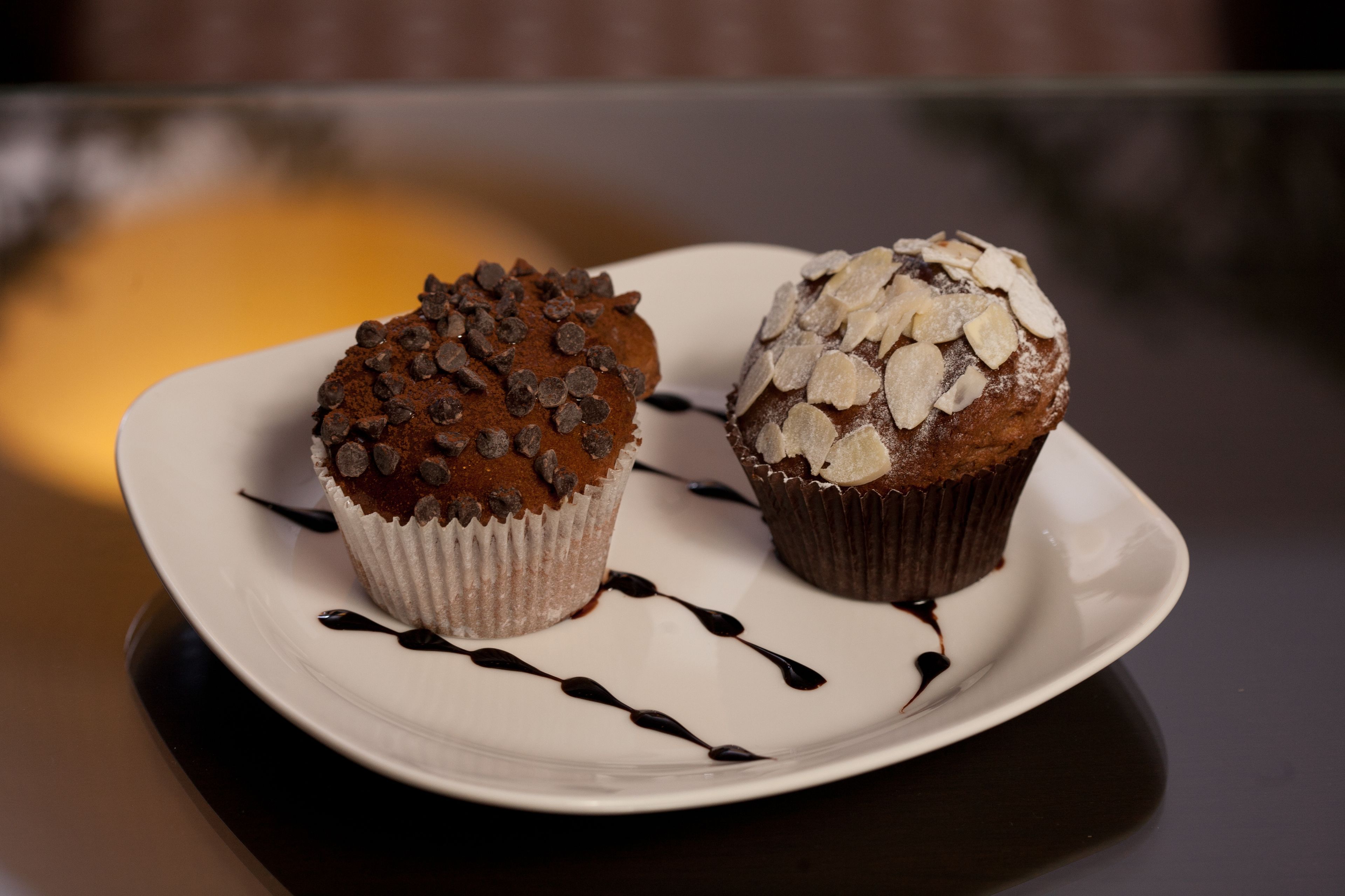 Two muffins on a white plate with chocolate chips and almond slices.