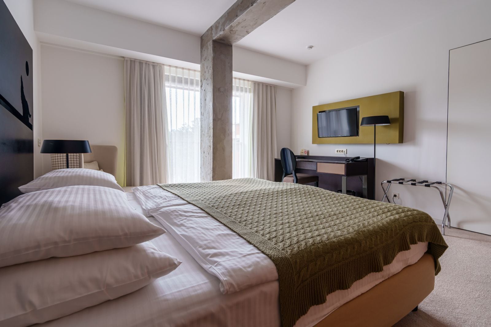 A hotel room with a large bed, a desk, a chair, a television, and a window with curtains.