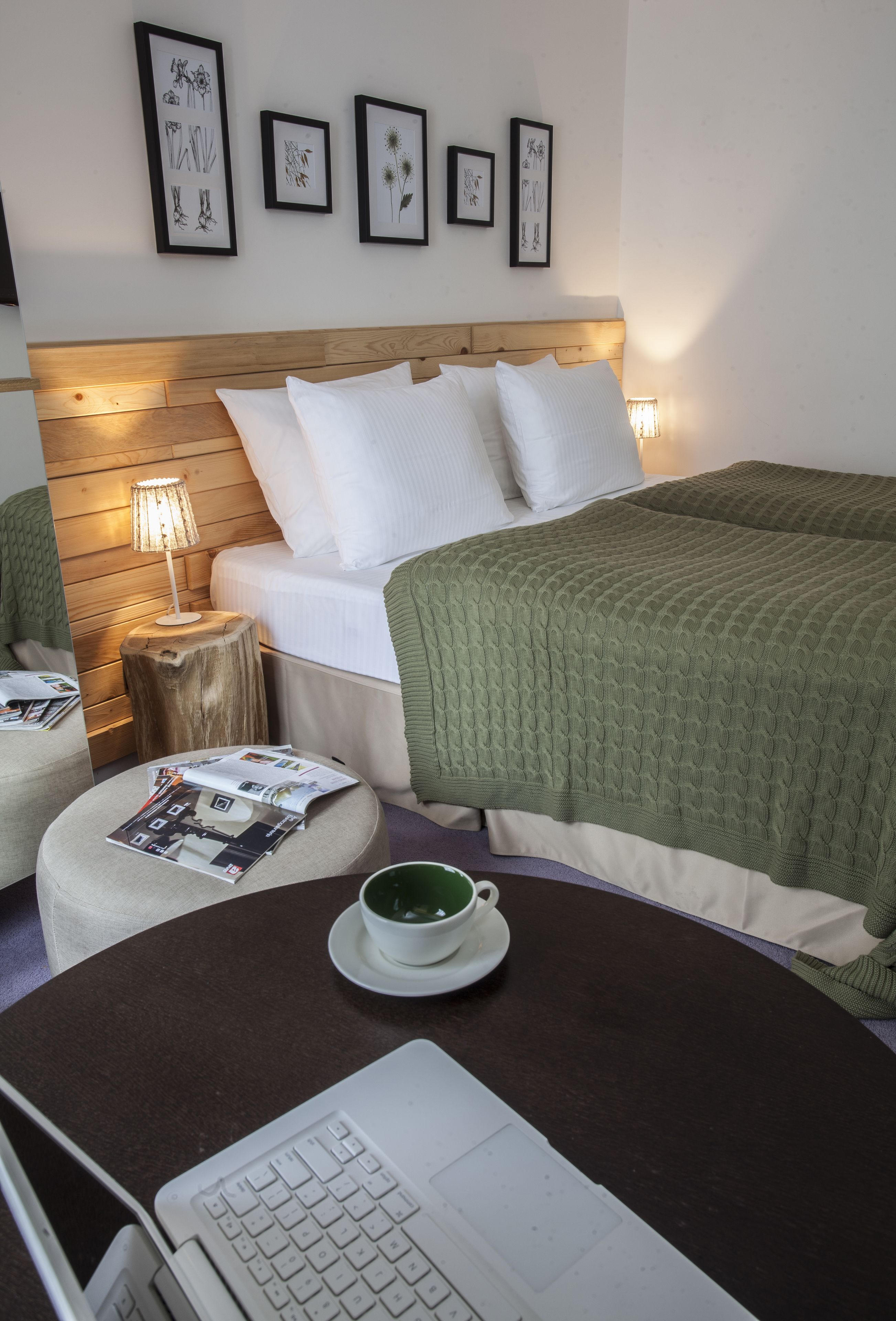 Een netjes ingerichte hotelkamer met een bed, een bedlampje, een klein rond tafeltje met een laptop en een beker.