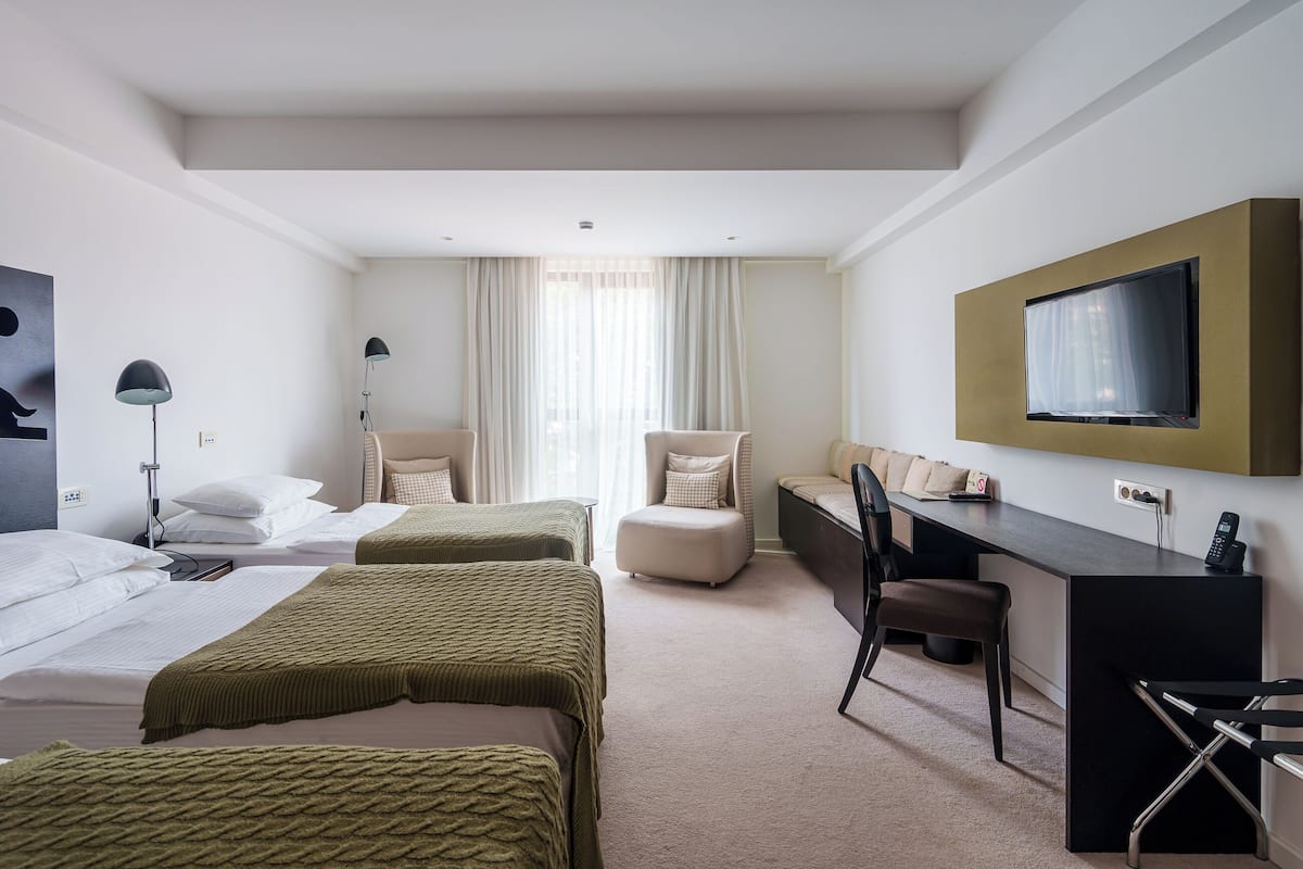 A hotel room with two beds, a desk, a chair, a TV, and a window with curtains.