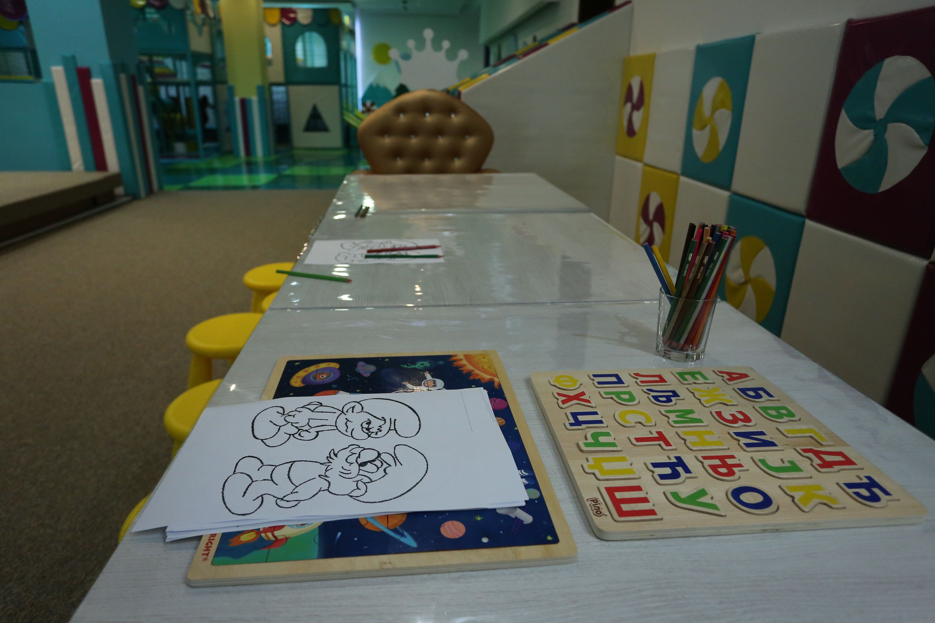 Una mesa larga con dibujos infantiles, fichas del alfabeto y lápices.