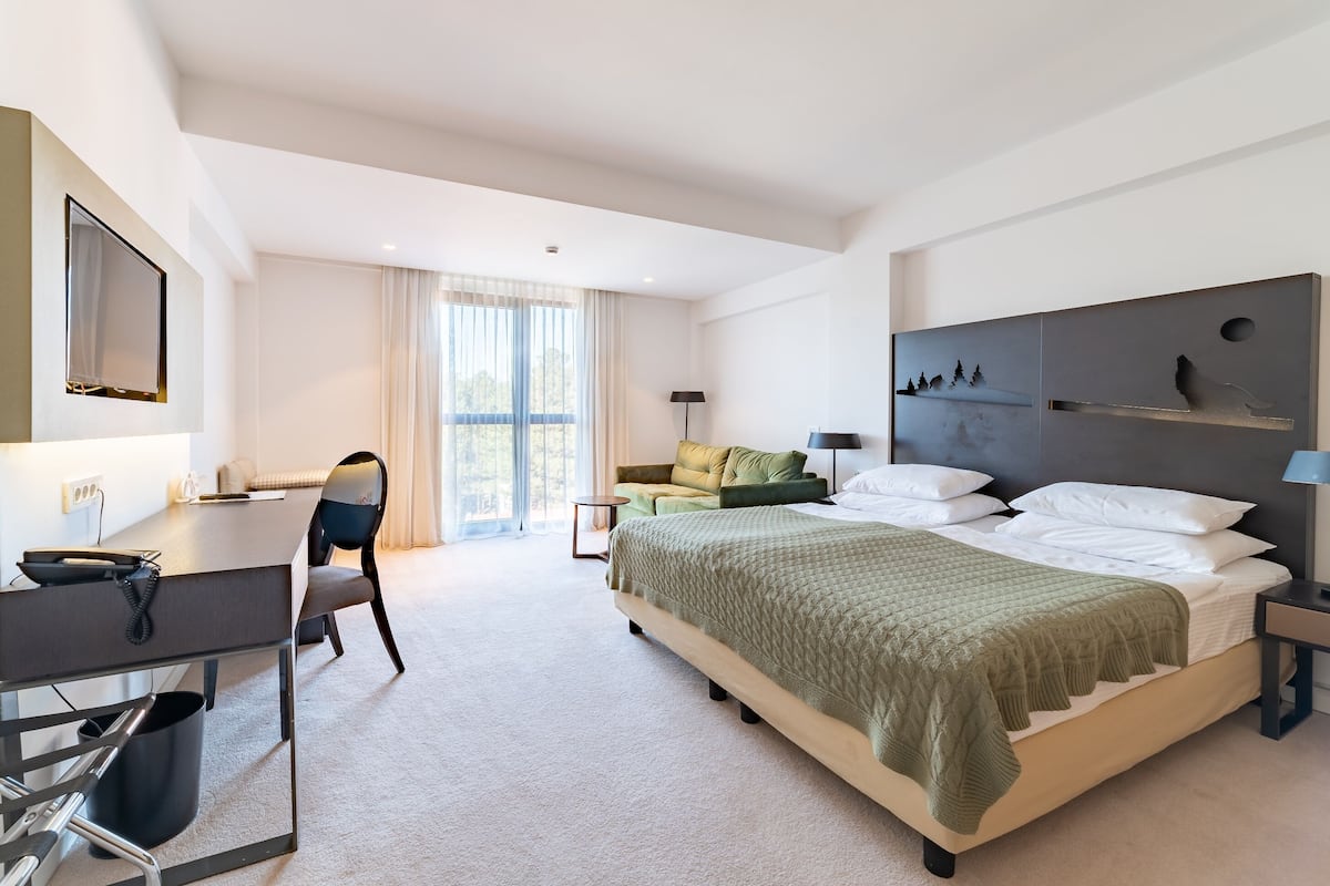 A modern hotel room with a large bed, a desk with a chair, a small table, and a sofa.