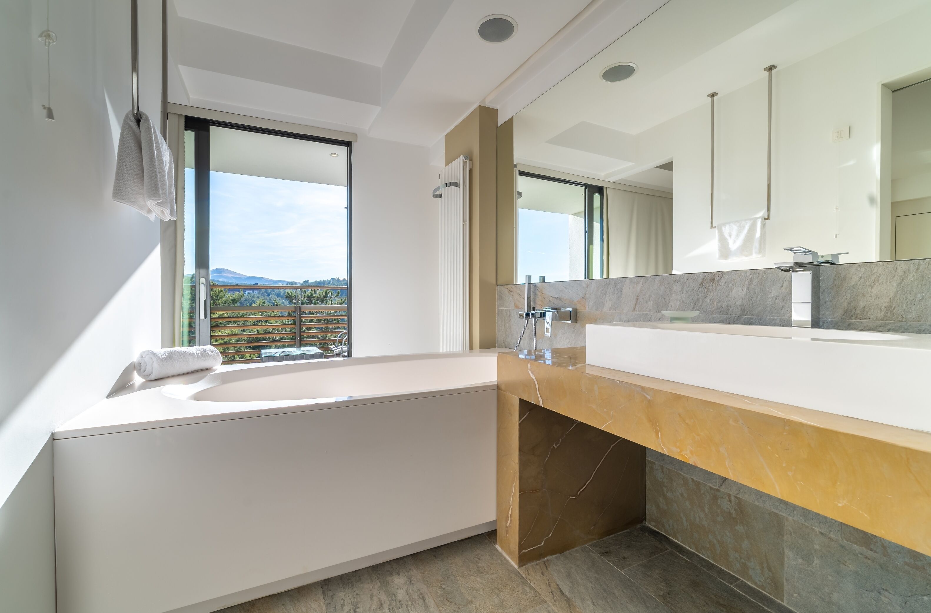 Un baño moderno con una bañera grande, un tocador con encimera de mármol y un espejo amplio.