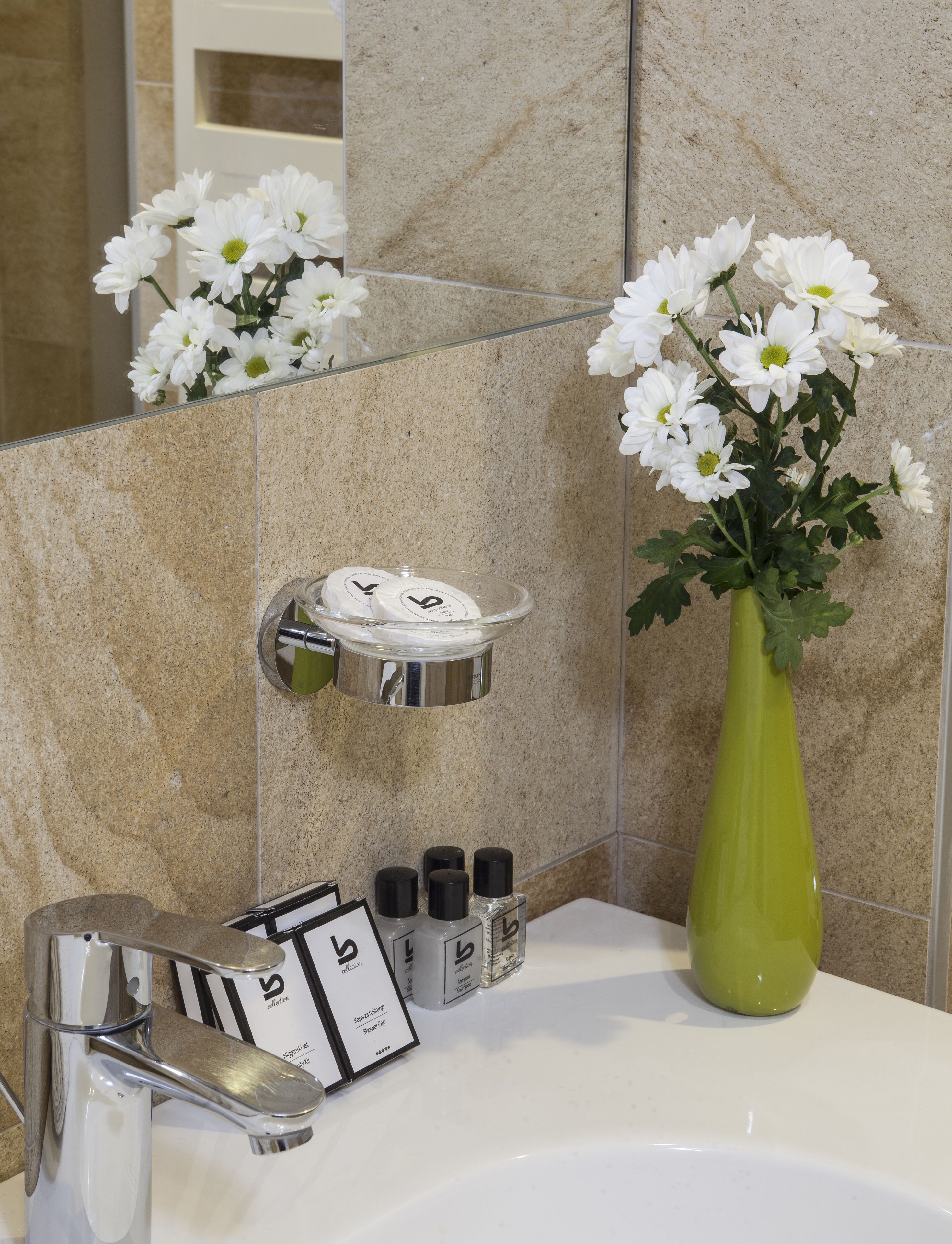 A bathroom with a sink, mirror, and a vase of white flowers. There are toiletries on the sink and a shower caddy on the wall.
