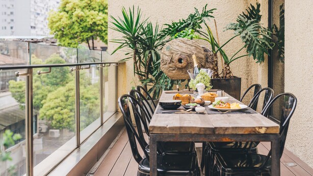 A balcony with a wooden table set for dining, surrounded by potted plants and a large decorative tree trunk. - Atour Hotel Jing'an The Drama Shanghai (Shanghai)